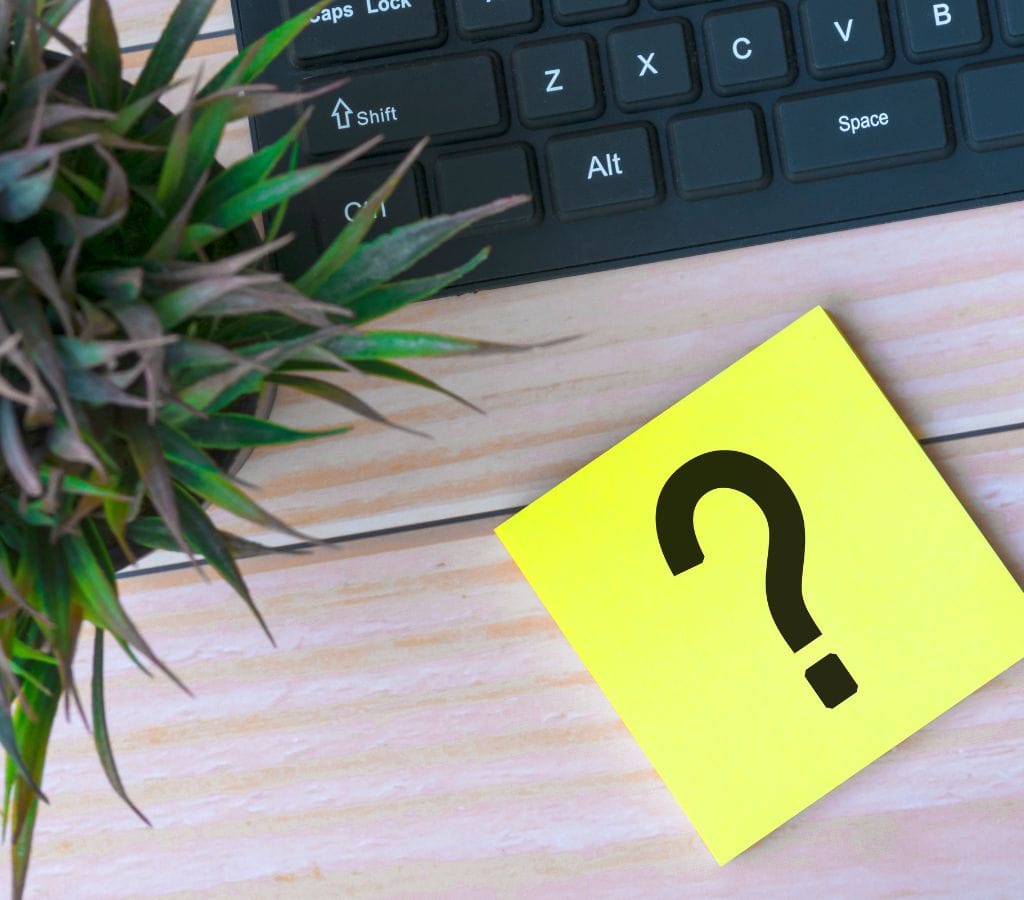 Question mark on adhesive note on wooden desk with keyboard