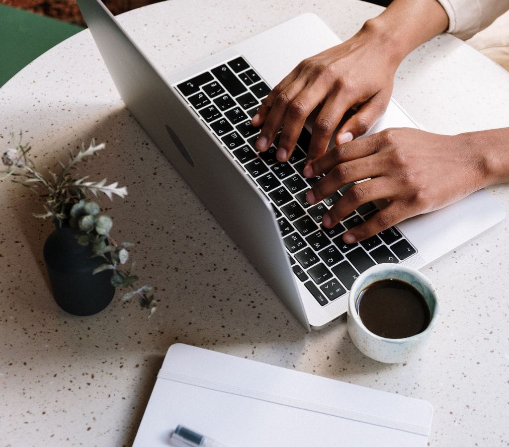 Person Using Macbook Pro Beside White Ceramic Mug