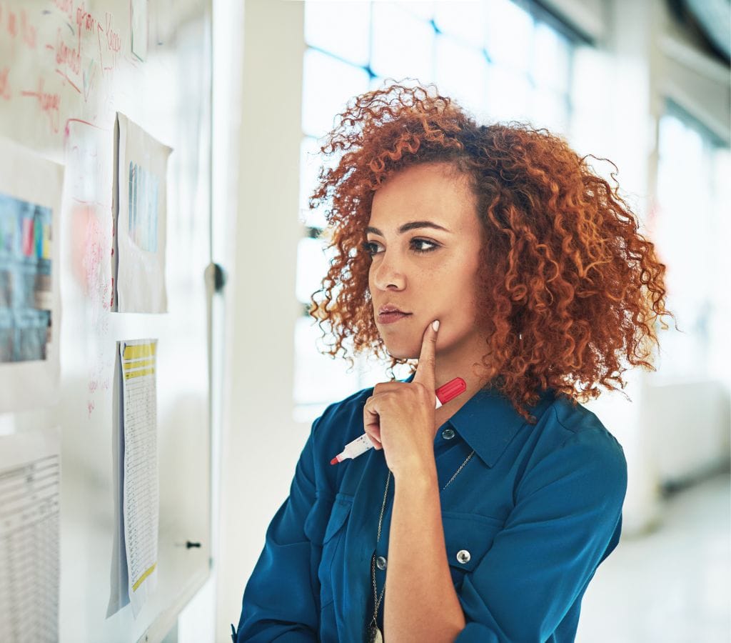 a woman thinking in front of a board while looking at a chart